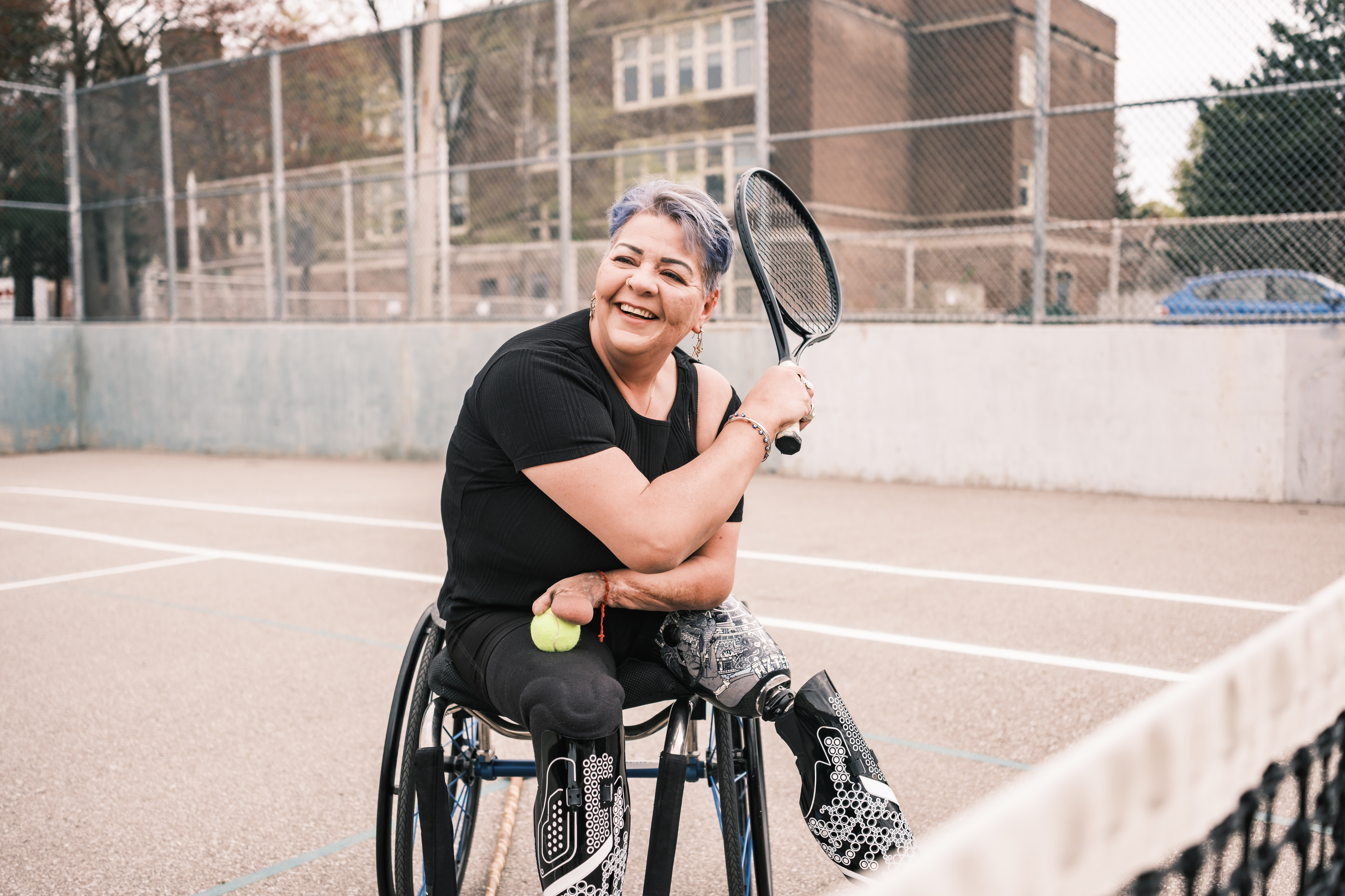 A middle aged woman in a wheelchair smiling and holding a tenis racket