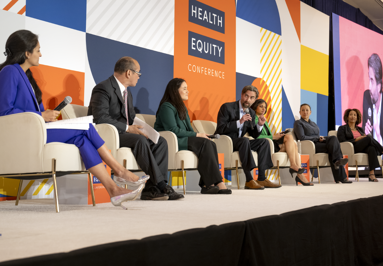 7 speakers sitting in a line on stage discussing